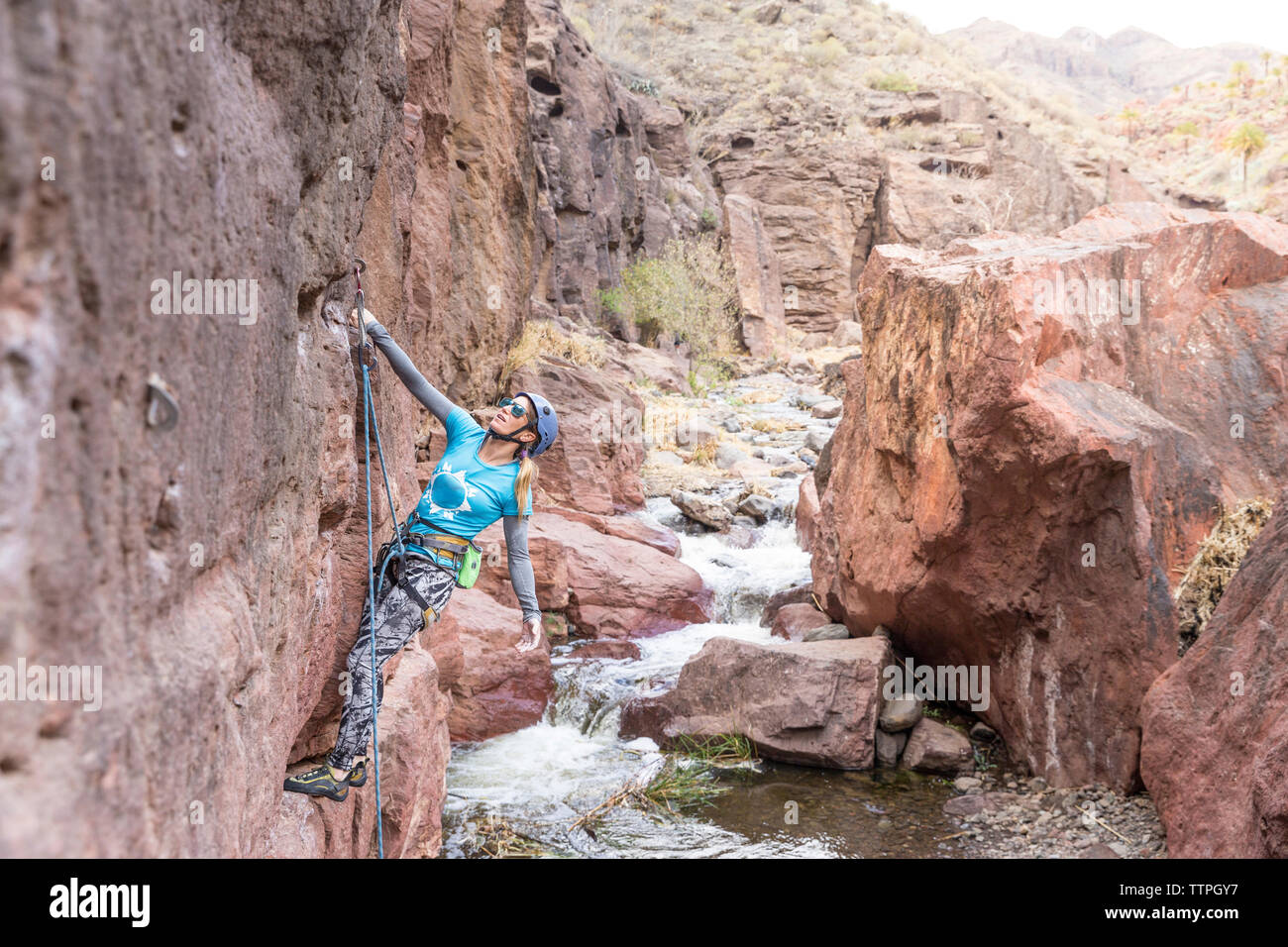 Female hiker using rope while climbing on rock formation by river Stock ...