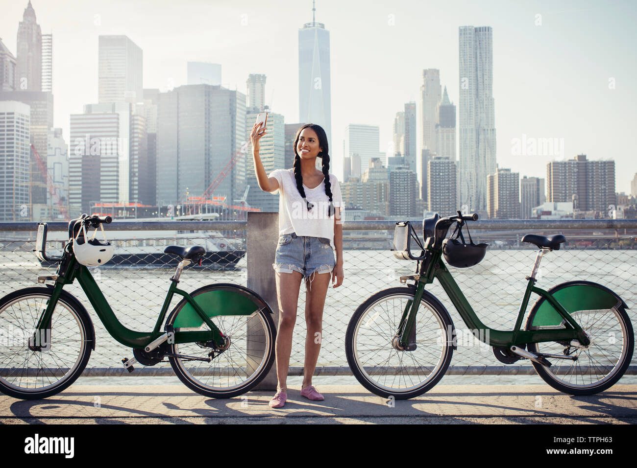 Happy woman taking selfie through mobile phone by bikes against cityscape Stock Photo