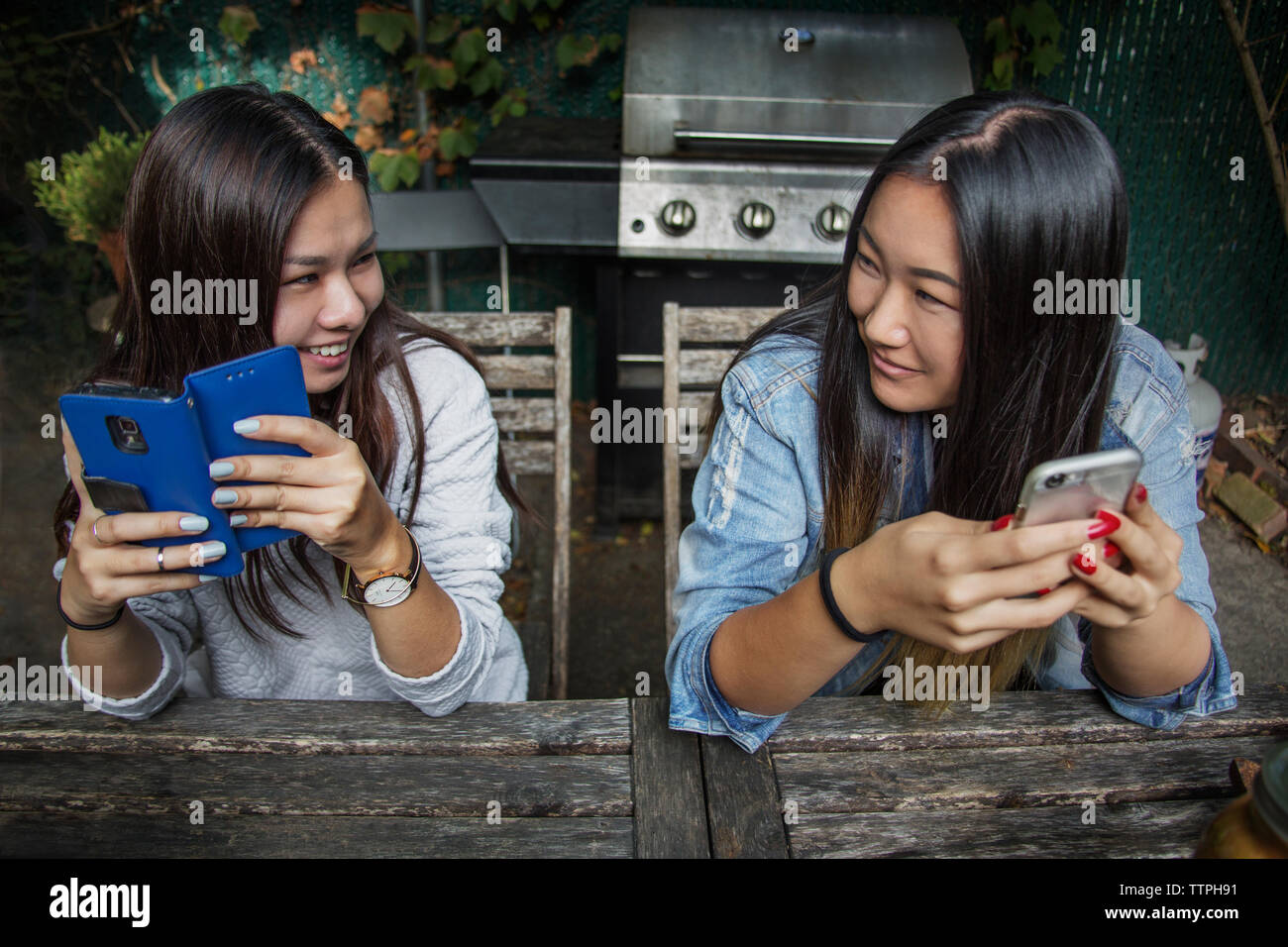 Happy female friend holding smart phone and looking face to face Stock Photo