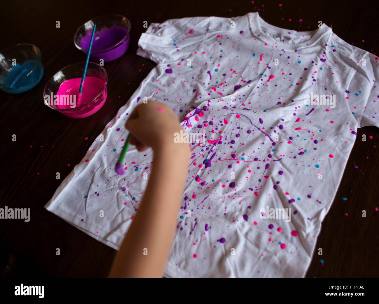 Cropped hand of girl splattering paint on t-shirt at home Stock Photo