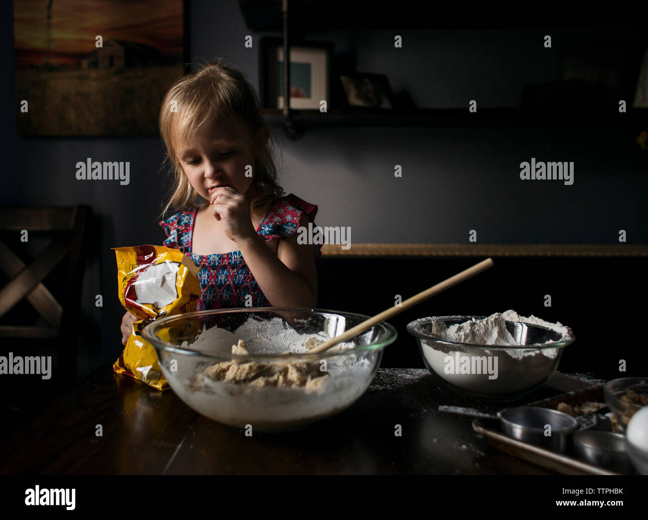 Girl eating while preparing food on table at home Stock Photo