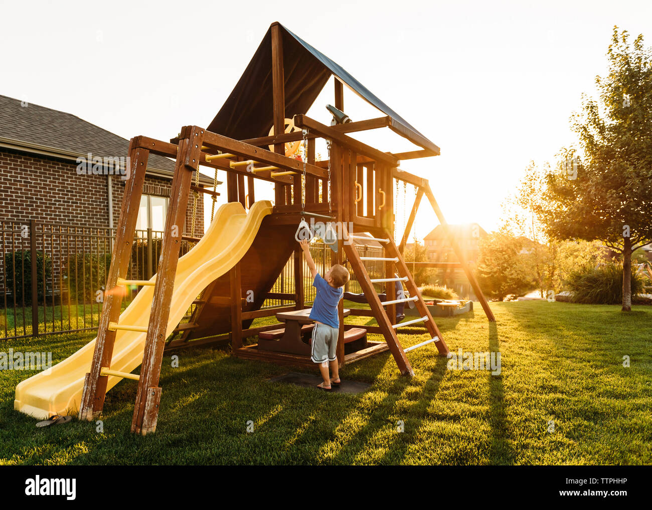 Boy playing with jungle gym in backyard during sunset Stock Photo