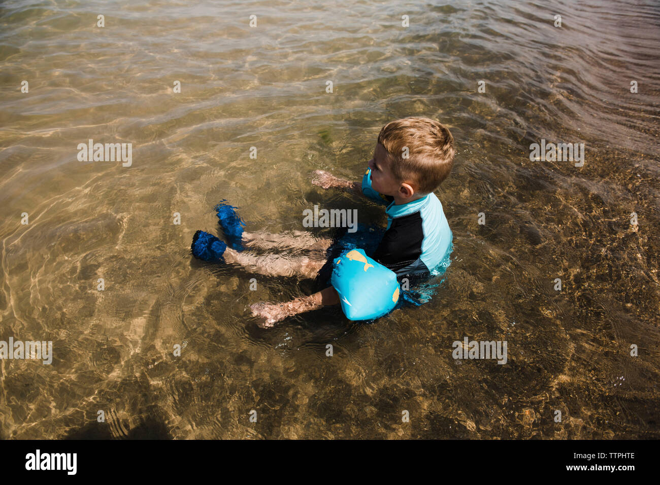 High angle view of boy with water wings sitting in sea Stock Photo