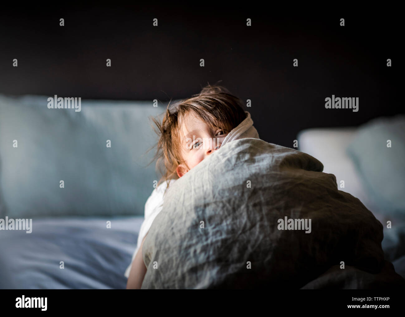 A Small Young Boy Playing Peek-A-Boo In A Bed With Blankets Stock Photo