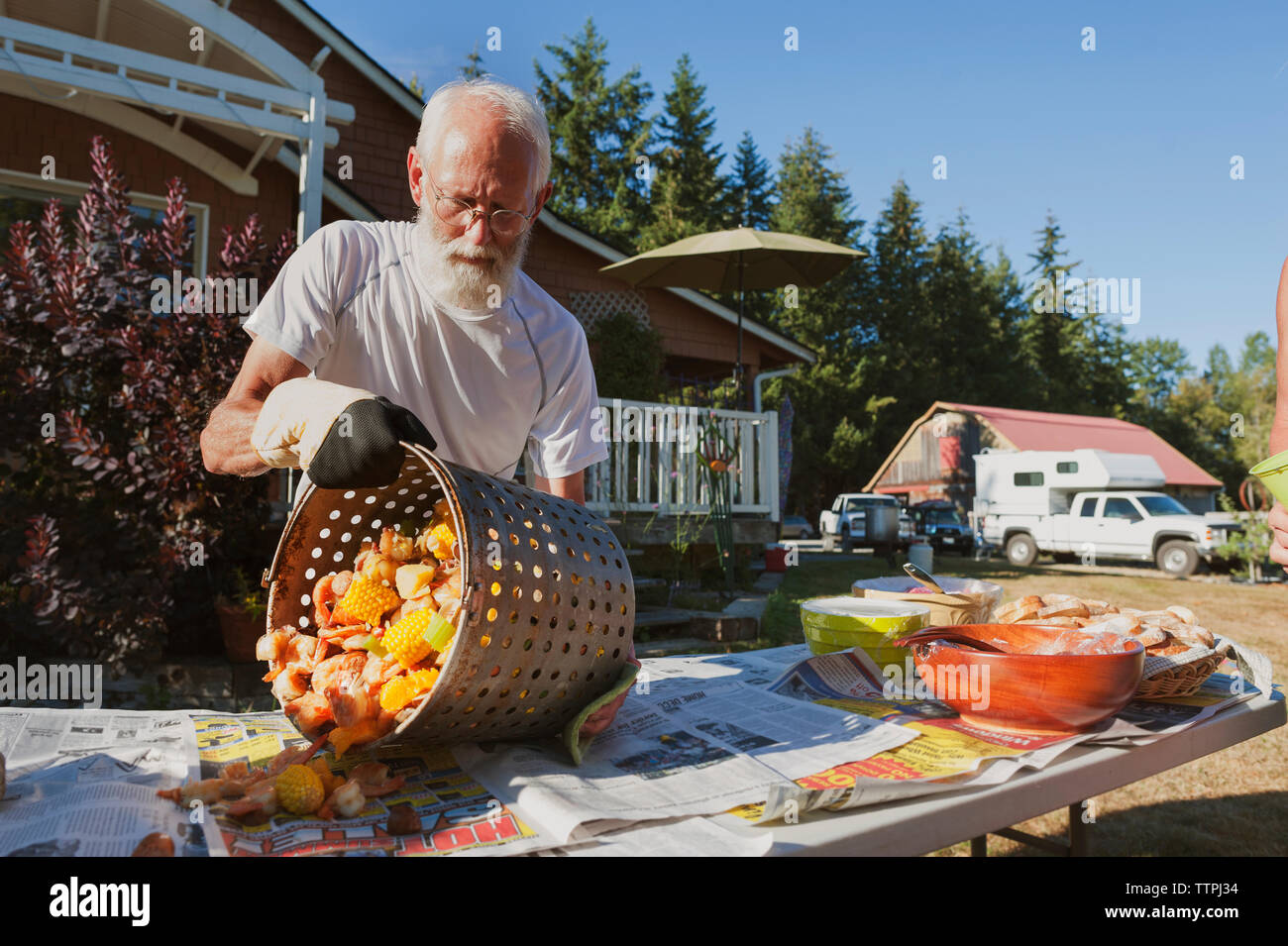 Man removing food from container on table in backyard against sky during sunny day Stock Photo