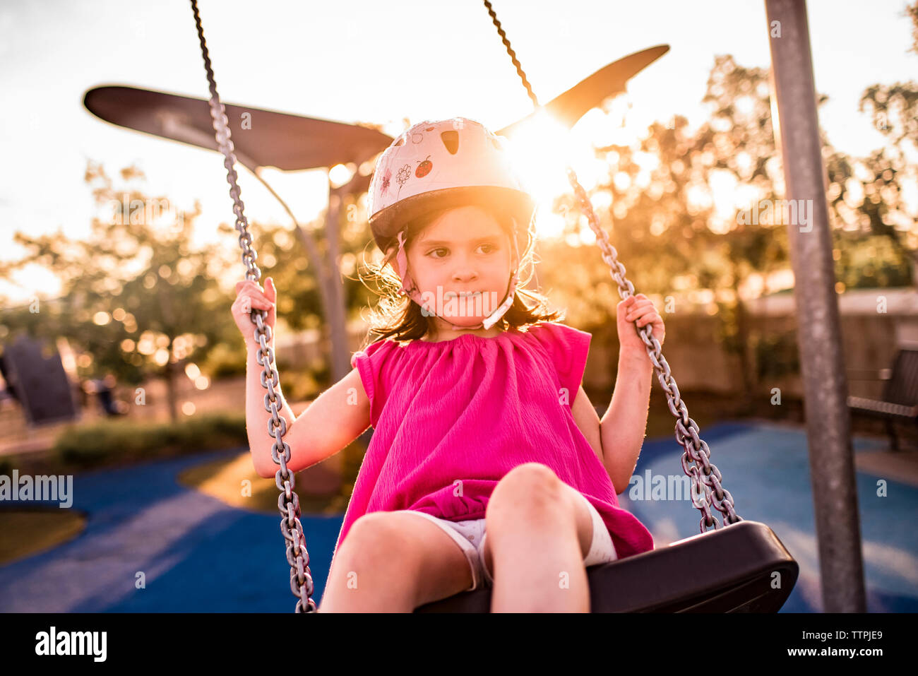 Girl wearing helmet while swinging at playground Stock Photo
