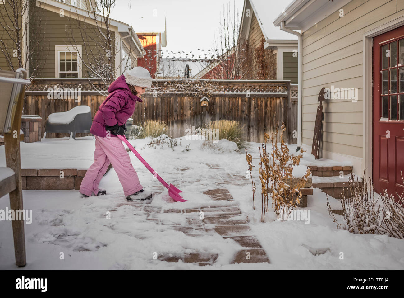 Side view of girl removing snow covered in backyard during winter Stock Photo
