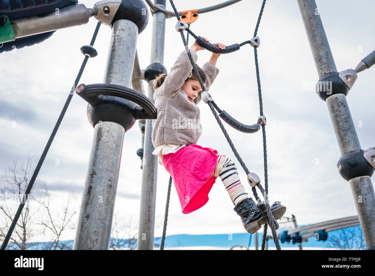 Low angle view of girl climbing on rope against cloudy sky at playground Stock Photo