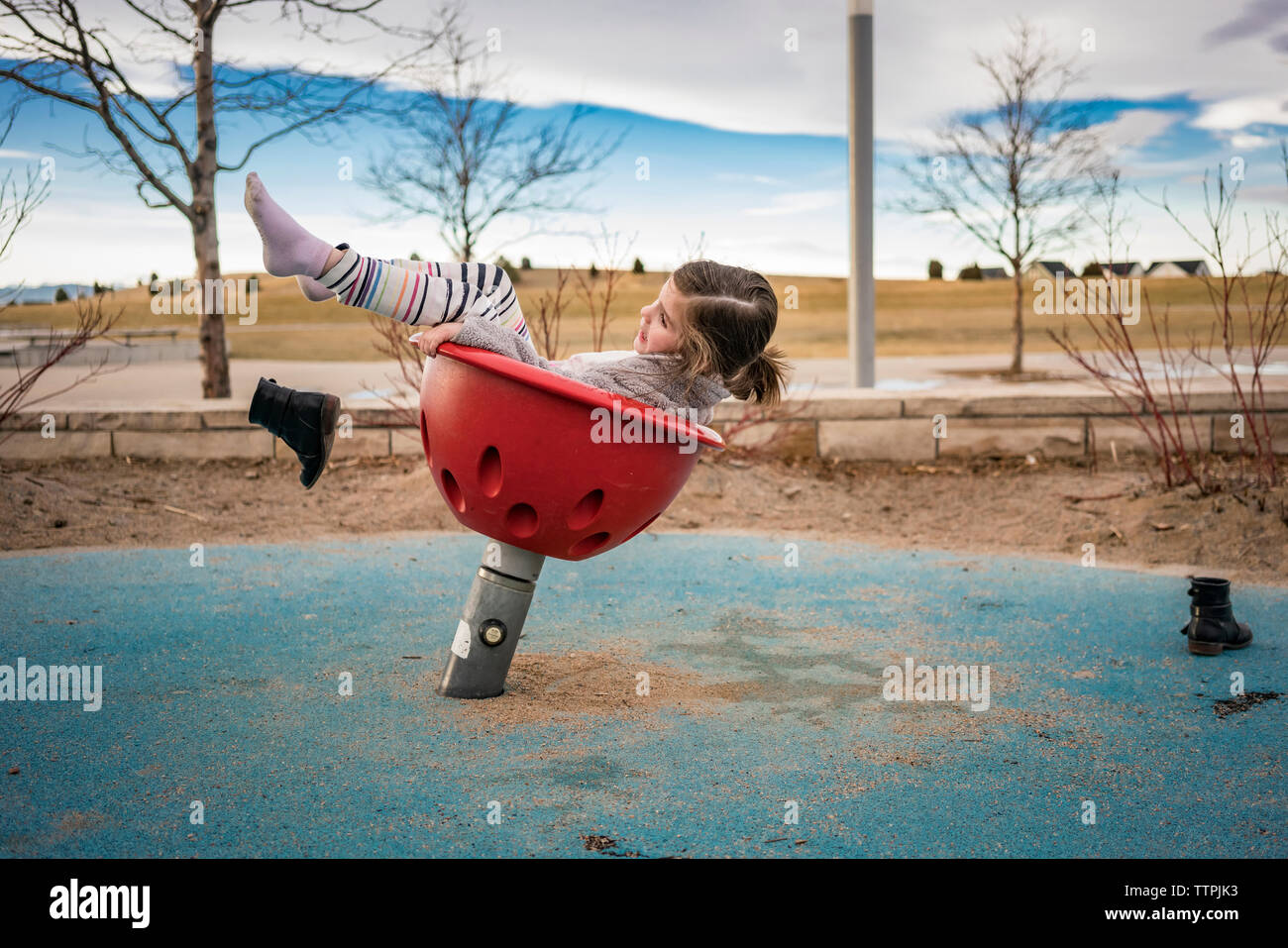 Side view of playful girl throwing shoes while playing on outdoor play equipment against cloudy sky at park Stock Photo