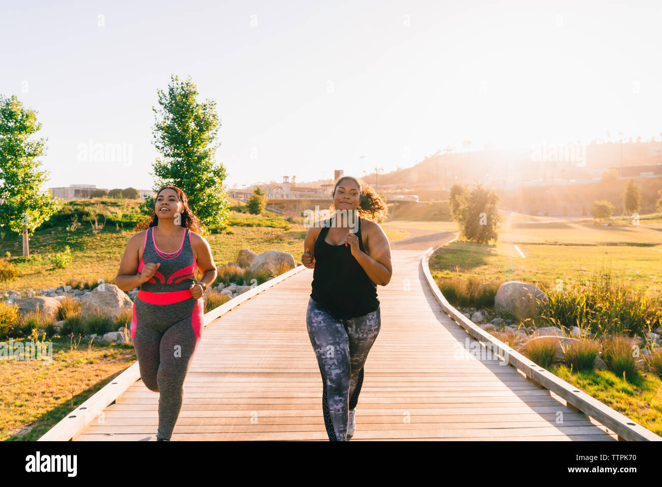 Sportswomen jogging on boardwalk against clear sky at park Stock Photo