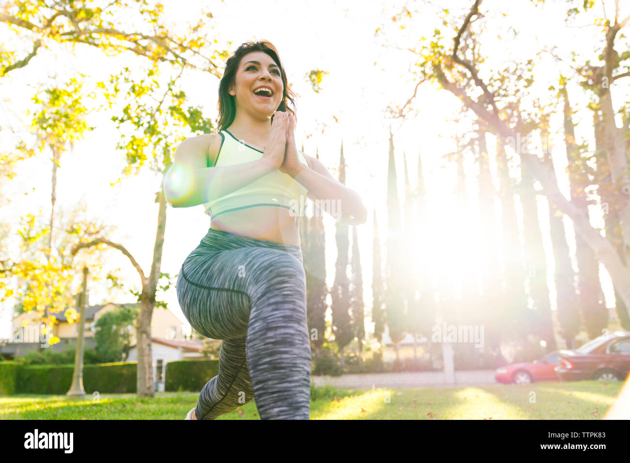 Low angle view of cheerful woman practicing yoga while exercising in park during sunny day Stock Photo