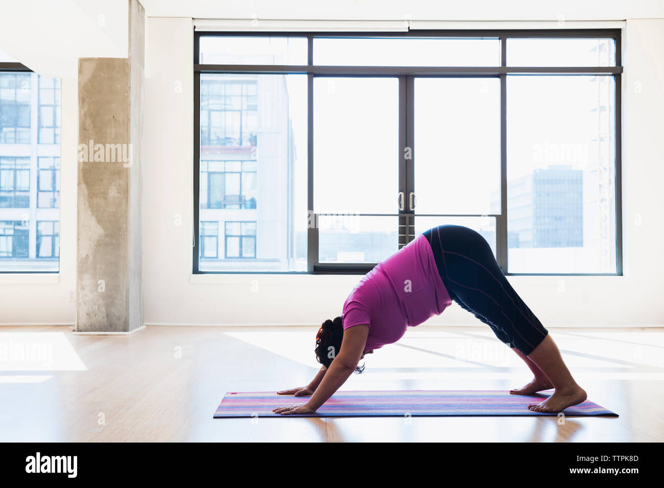 Side view of woman practicing downward facing dog position yoga against window Stock Photo