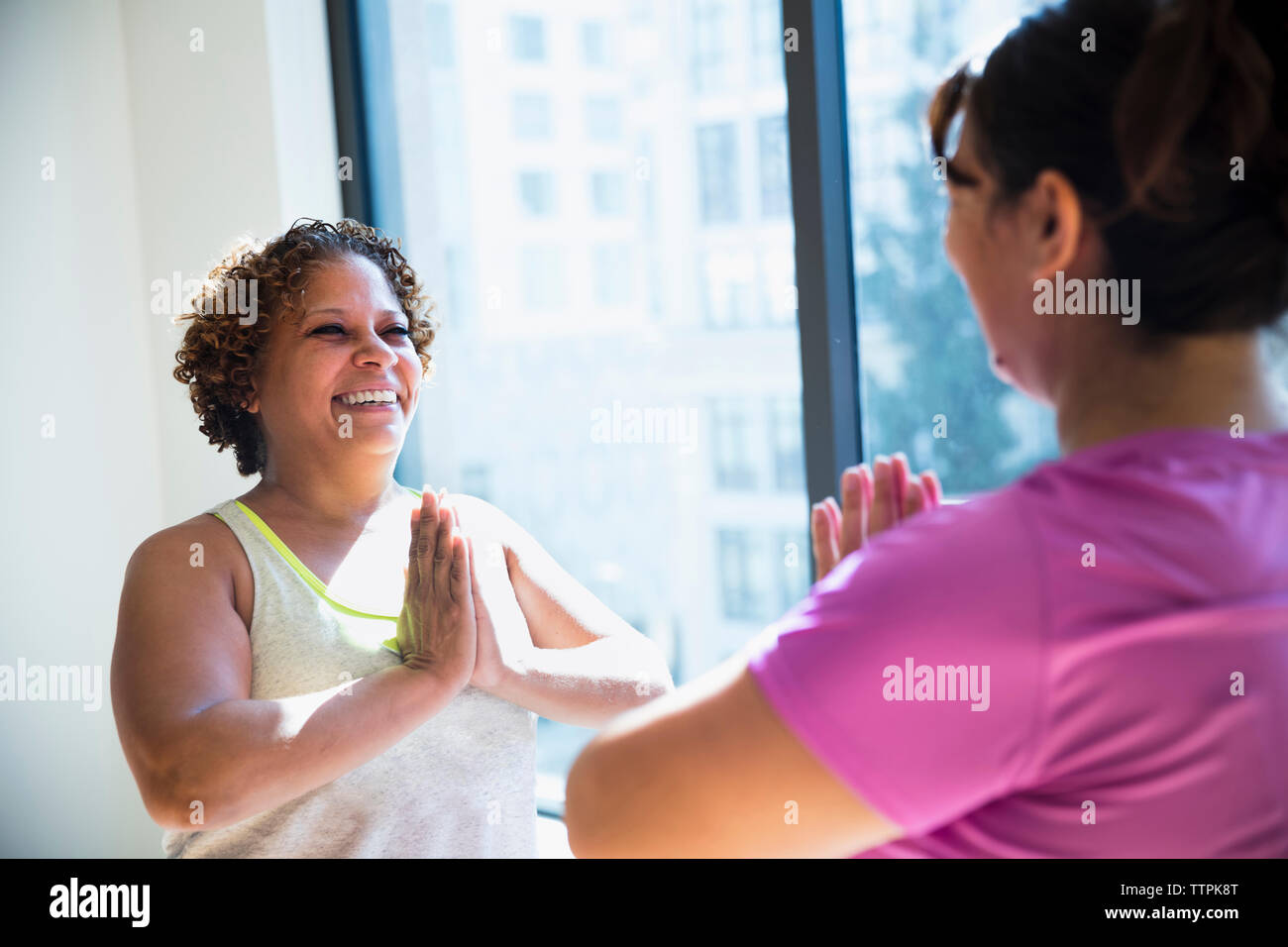 Happy friends with hands clasped exercising face to face in yoga studio Stock Photo