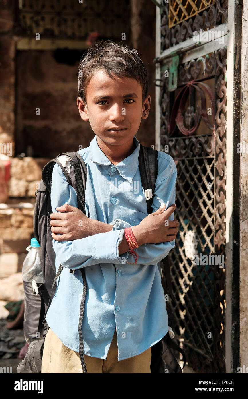 Portrait of boy with arms crossed and backpack wearing school uniform by gate against house Stock Photo