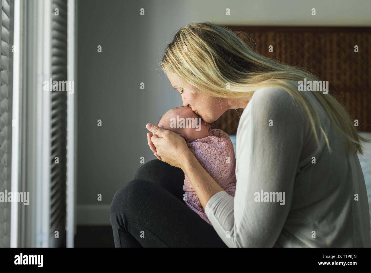 Side view of mother kissing newborn daughter while carrying her at home Stock Photo