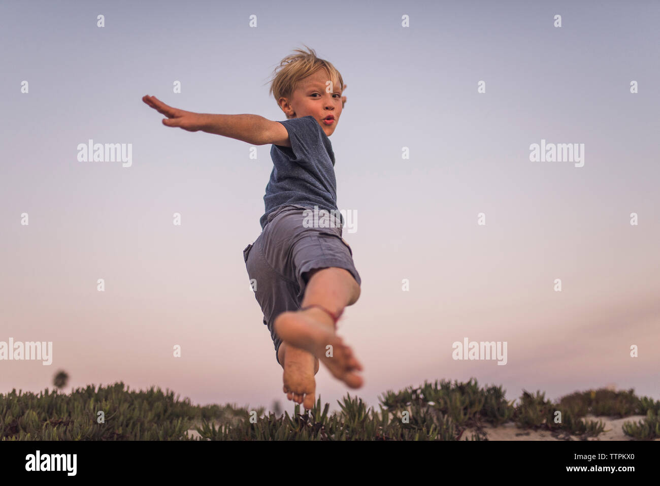 Low angle view of boy jumping on sand at beach against sky during sunset Stock Photo