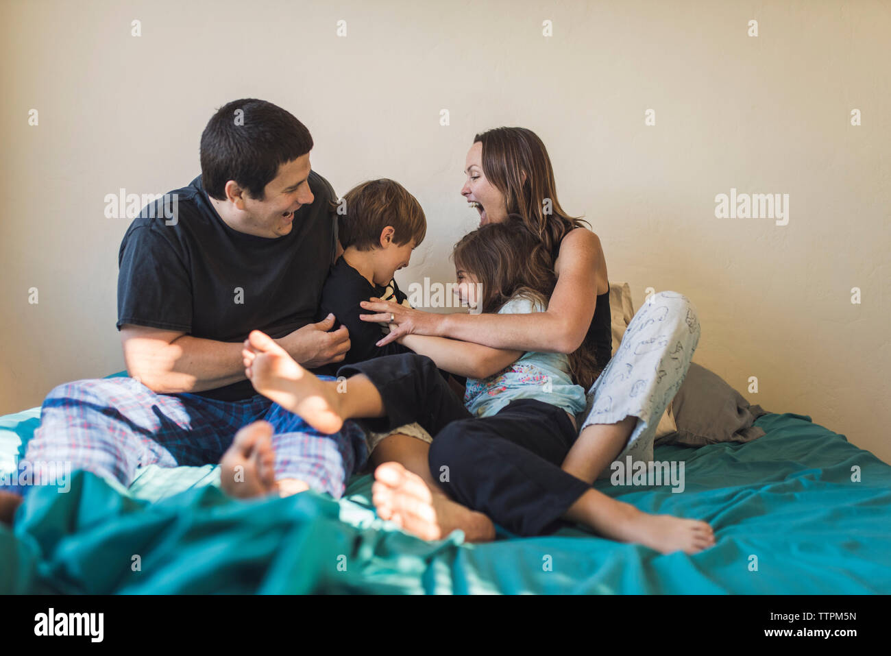 Cheerful parents playing with children on bed at home Stock Photo