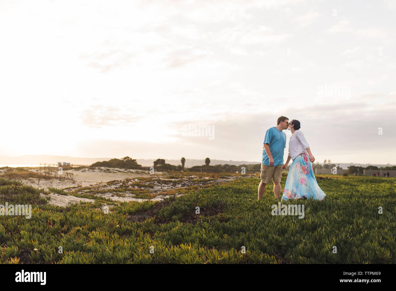 Couple kissing while standing on field against sky Stock Photo
