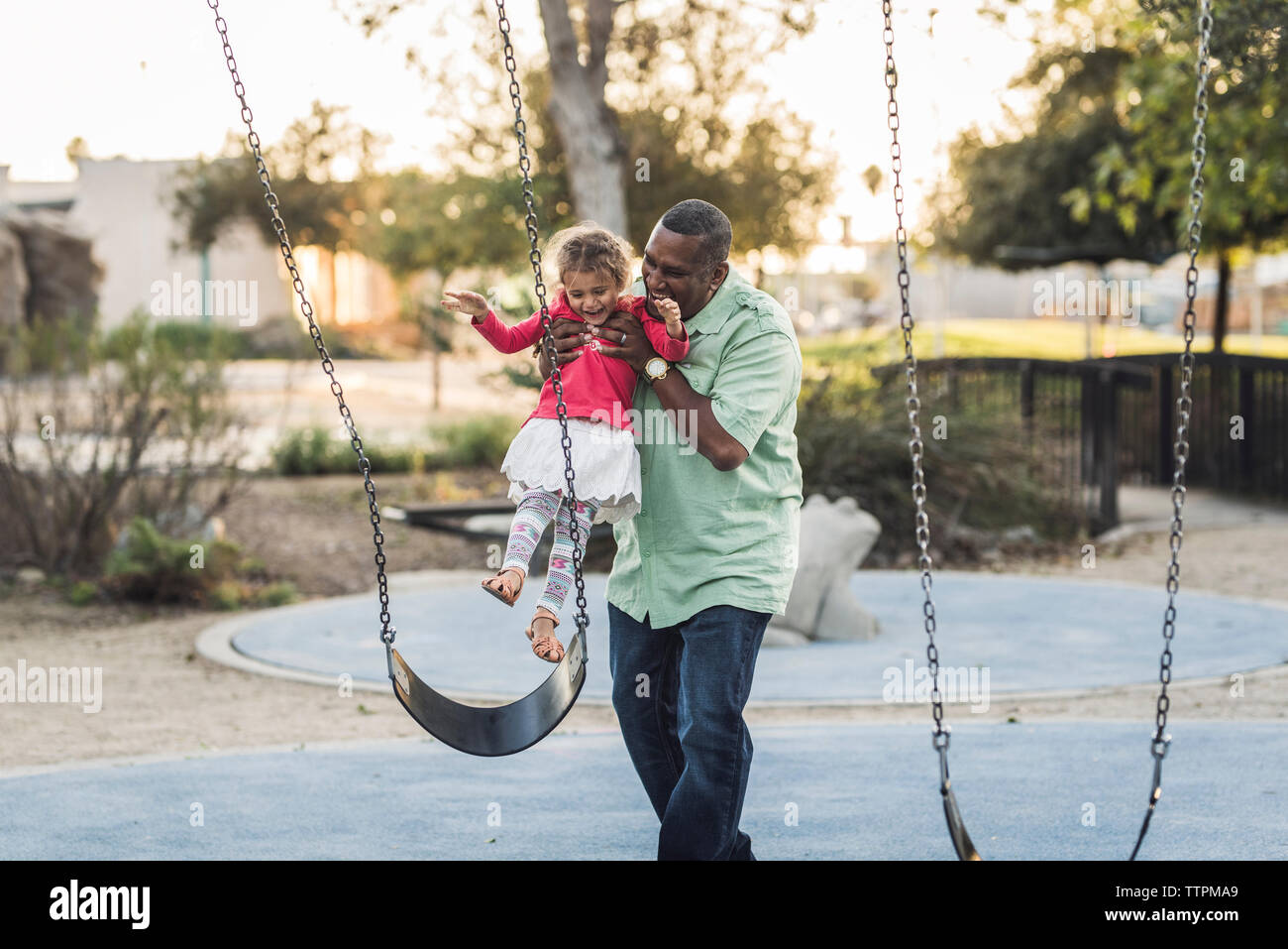 Playful father picking up daughter from swing while playing at playground Stock Photo