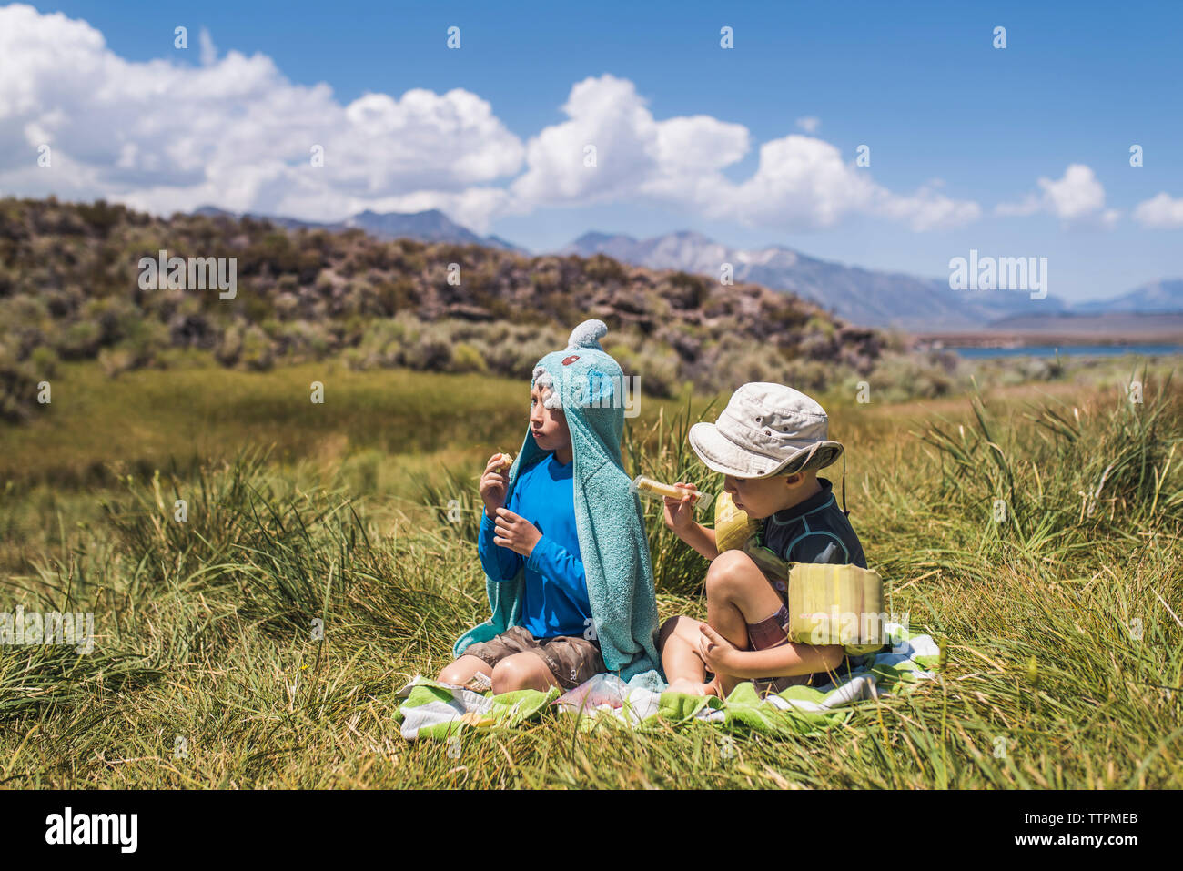 Carefree brothers sitting on grassy field during sunny day Stock Photo