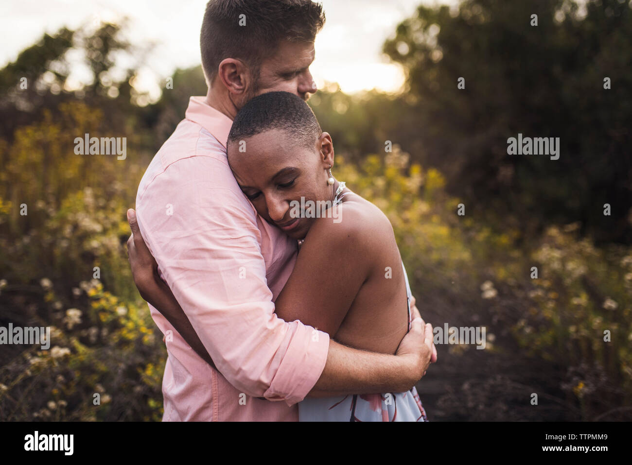 Side view of romantic couple embracing against plants in park during sunset Stock Photo