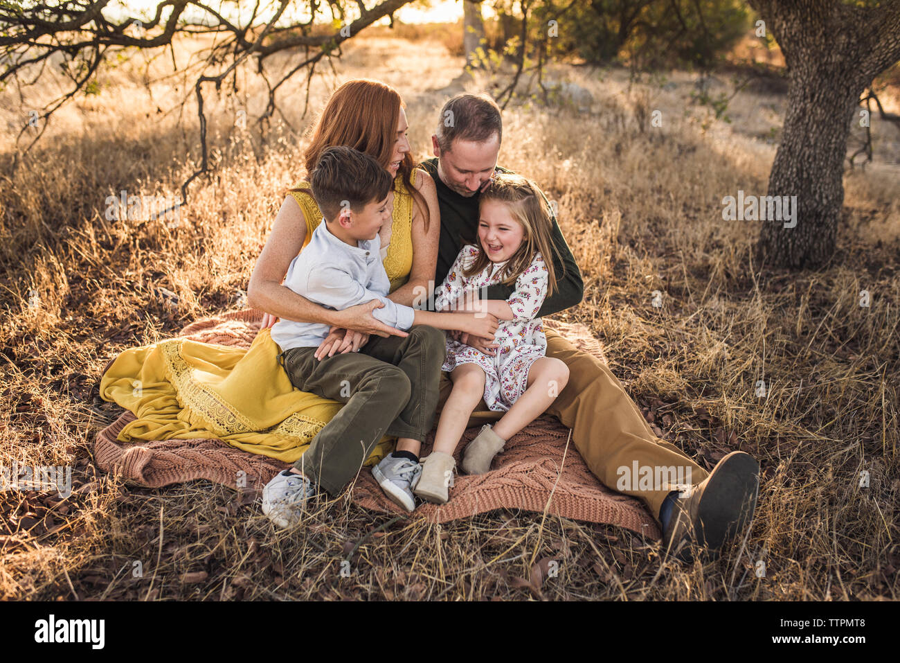 Young family sitting and tickling daughter while embracing/laughing Stock Photo