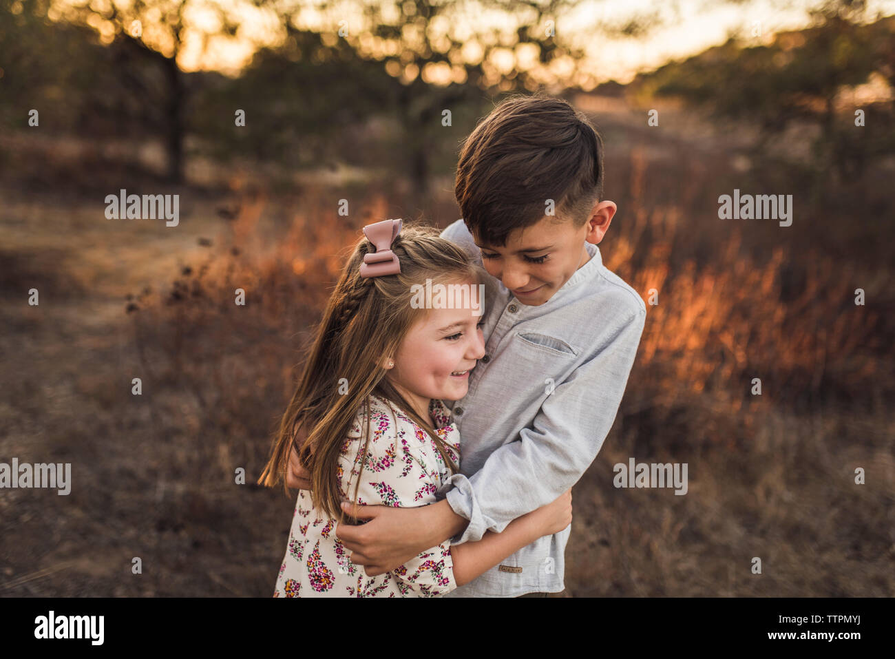 Young girl and boy embracing in California field at sunset Stock Photo