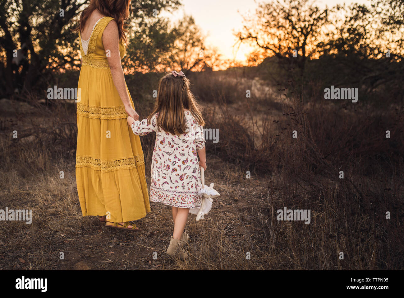 Young girl holding mothers hand while walking away in California field Stock Photo