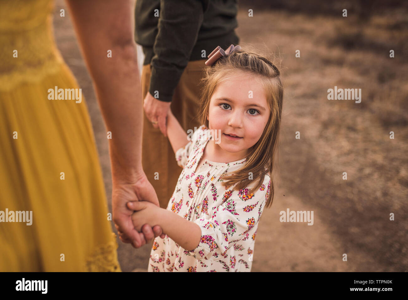 Young girl holding parents hand in California field at sunset Stock Photo