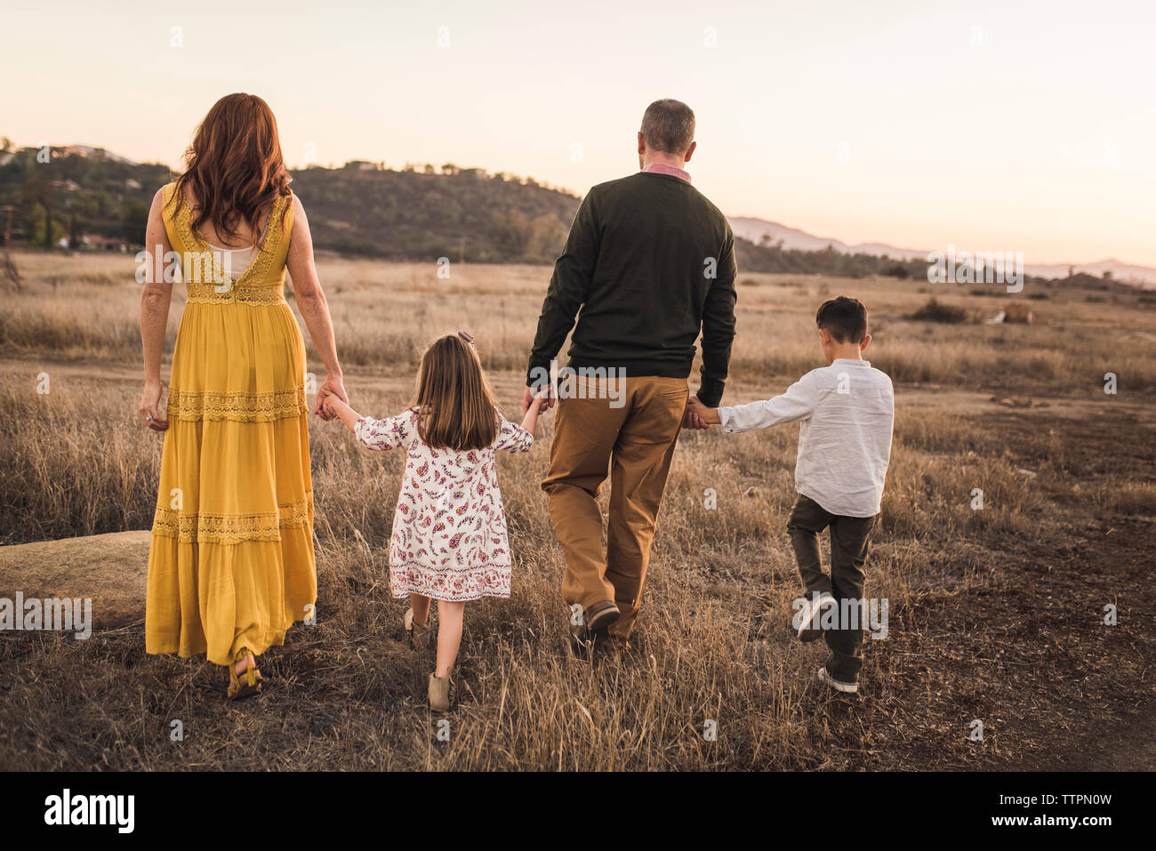 Young family holding hands while walking away in California field Stock Photo
