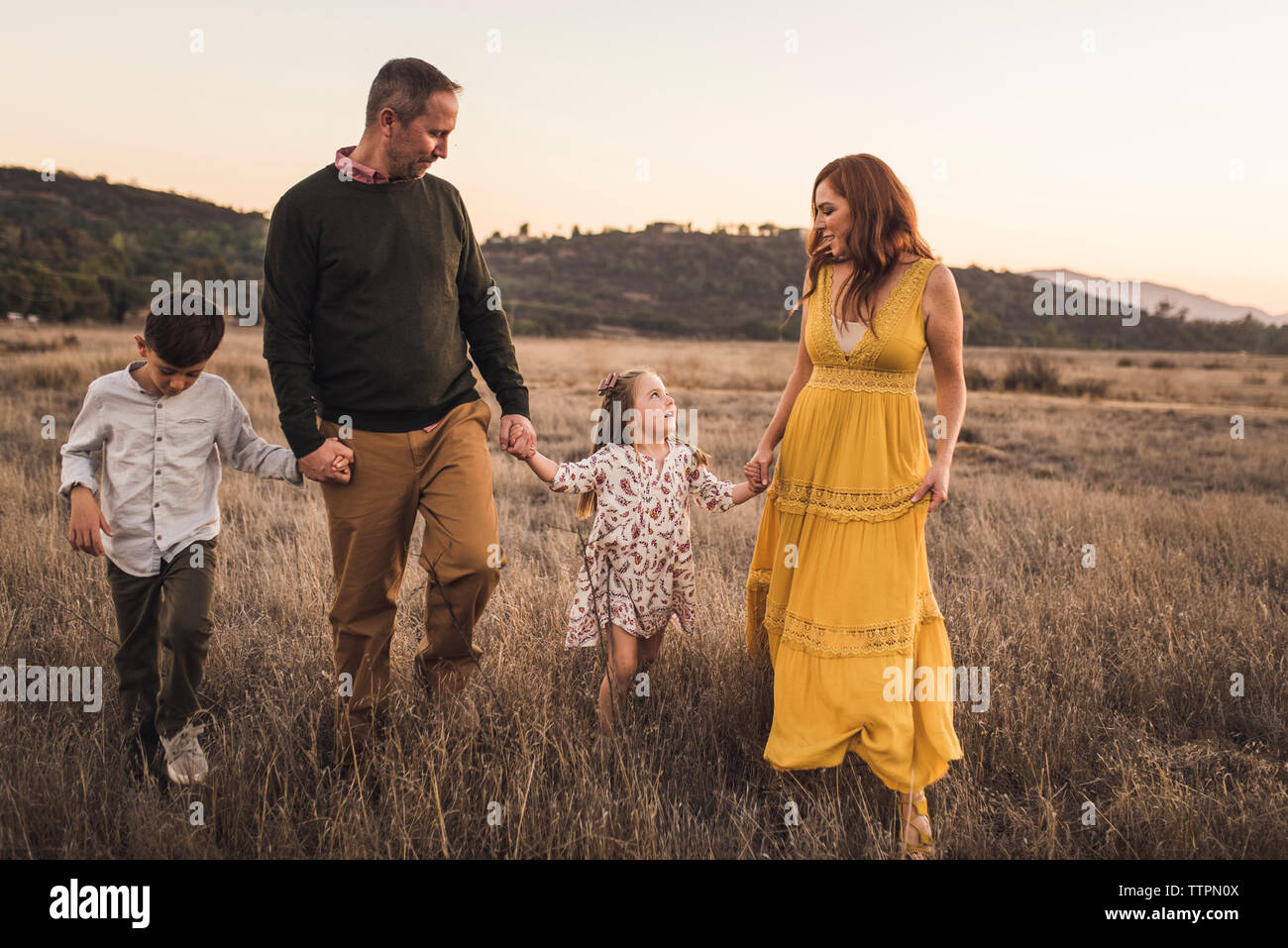 Young family holding hands while walking in California field at sunset Stock Photo
