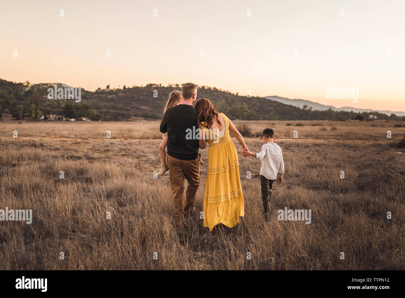 Young family holding hands while walking away in California field Stock Photo