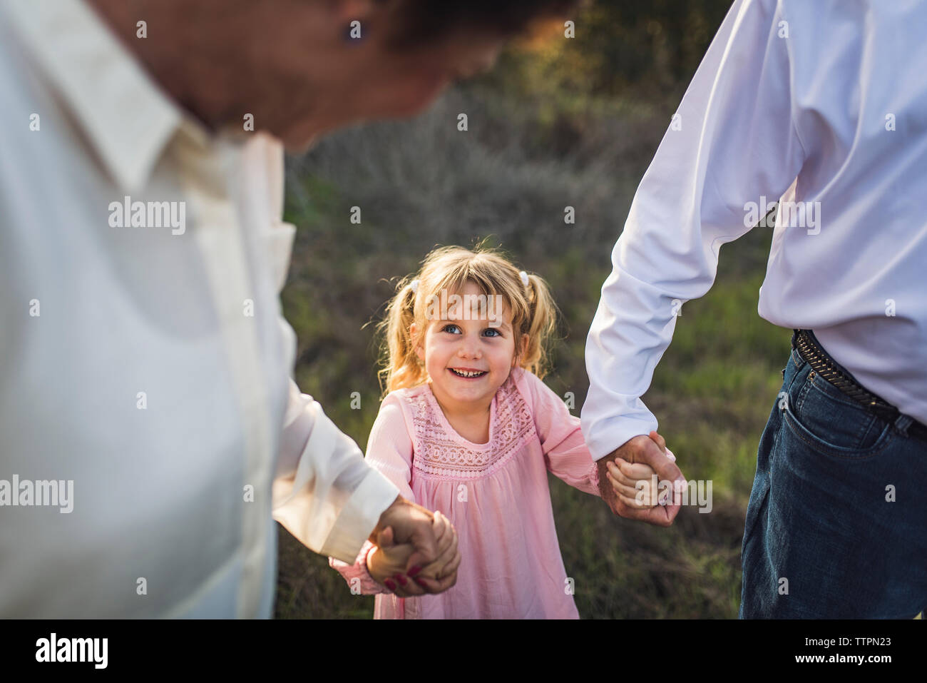 Little girl holding hands with grandparents, looking up and smiling Stock Photo