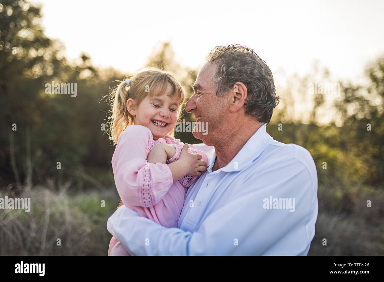 Grandpa holding granddaughter in field and laughing Stock Photo
