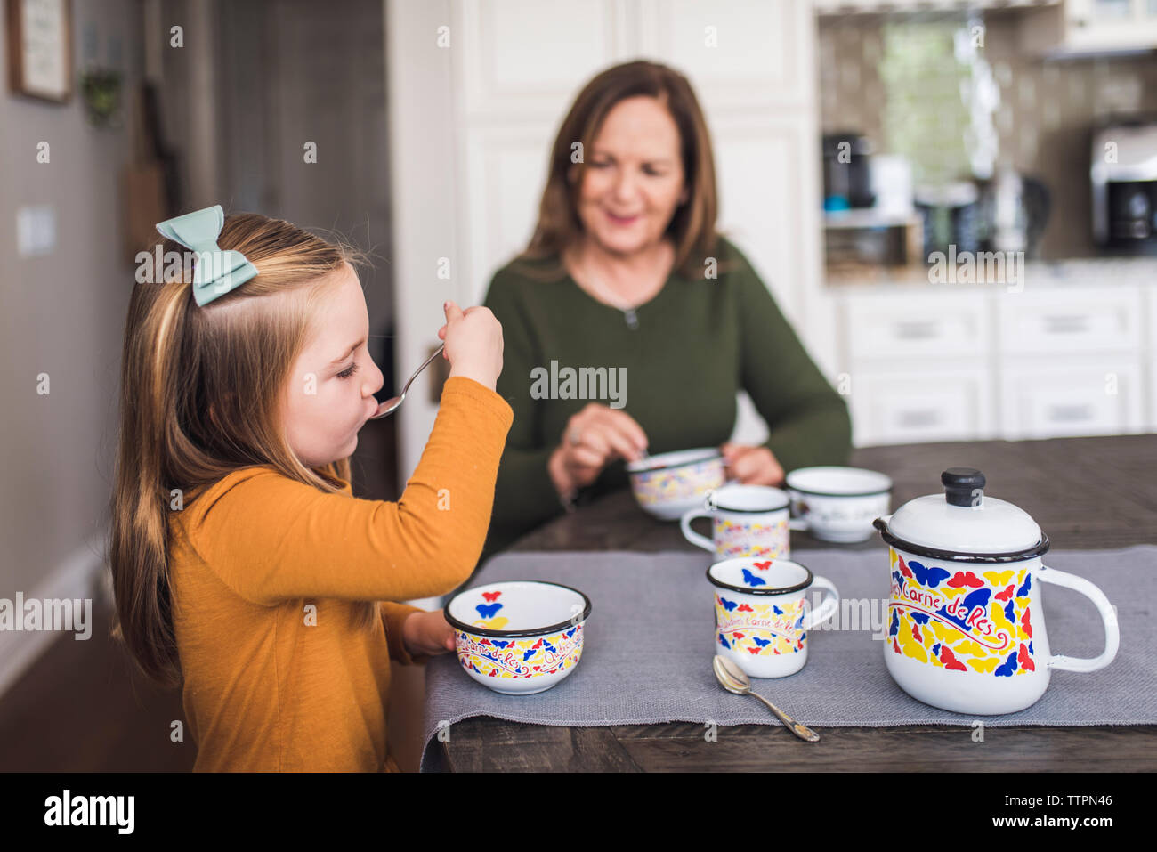 Granddaughter and grandmother in kitchen playing with tea set Stock Photo