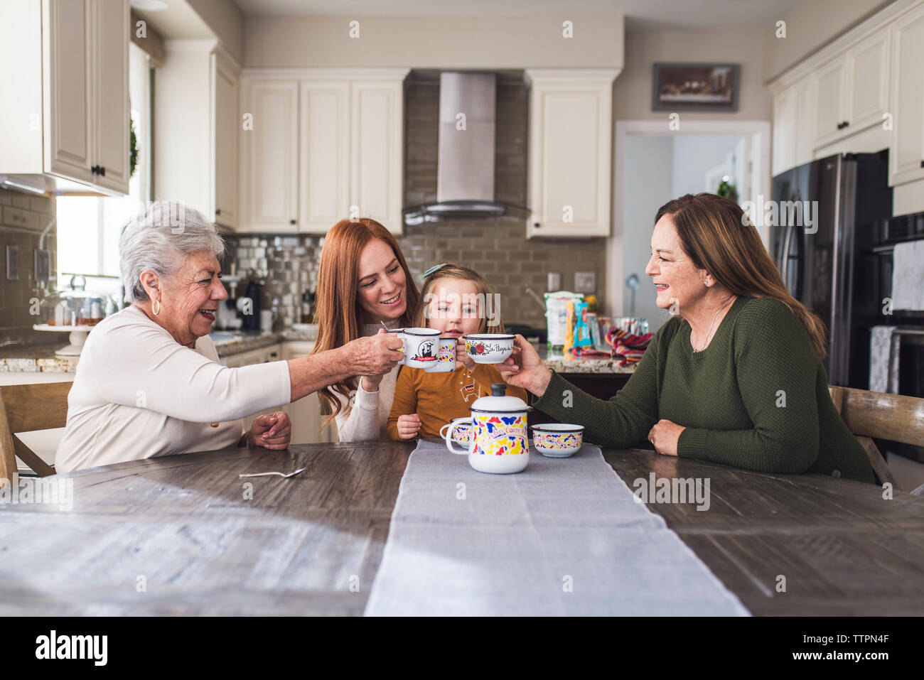 Multigenerational family cheersing with tea set at kitchen table Stock Photo