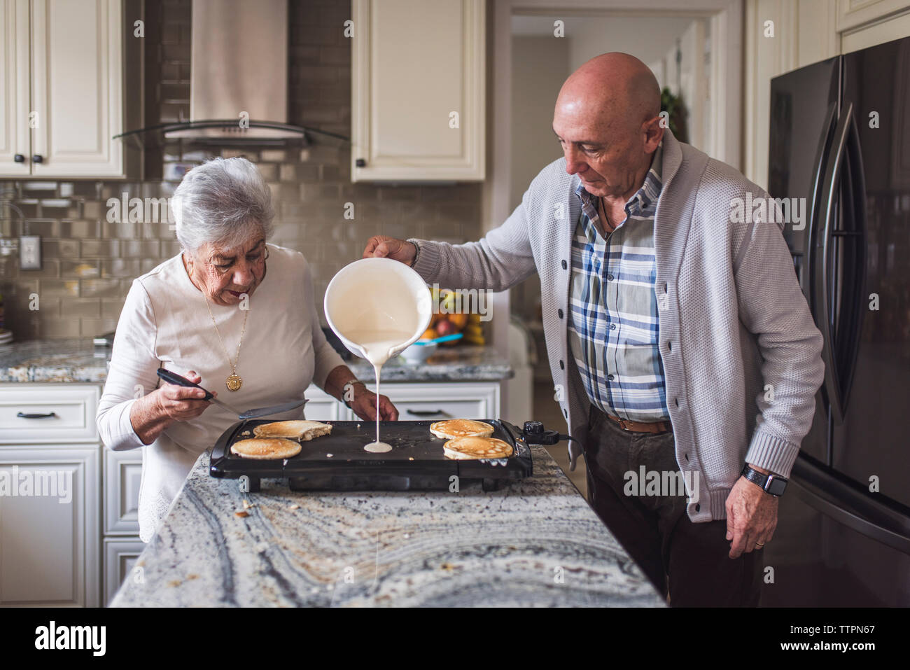 Great grandma cooking pancakes with her adult son Stock Photo