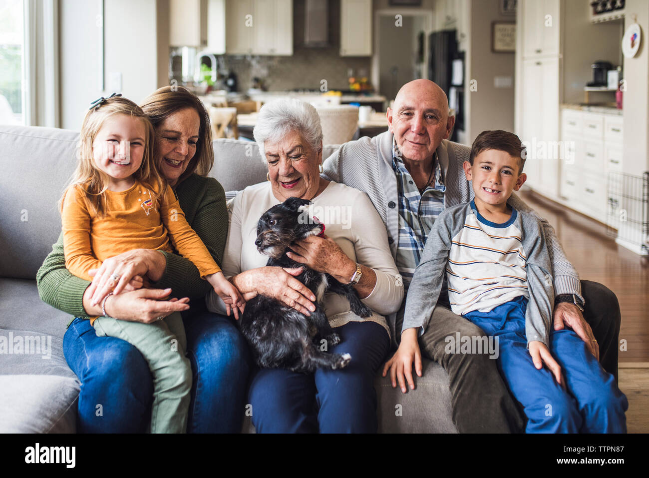 Multigenerational family and small dog sitting on living room couch Stock Photo