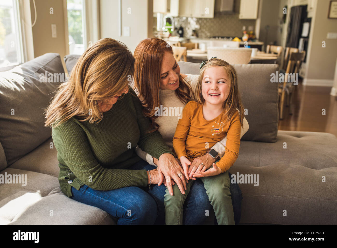 Portrait of three generations of women sitting on living room couch Stock Photo