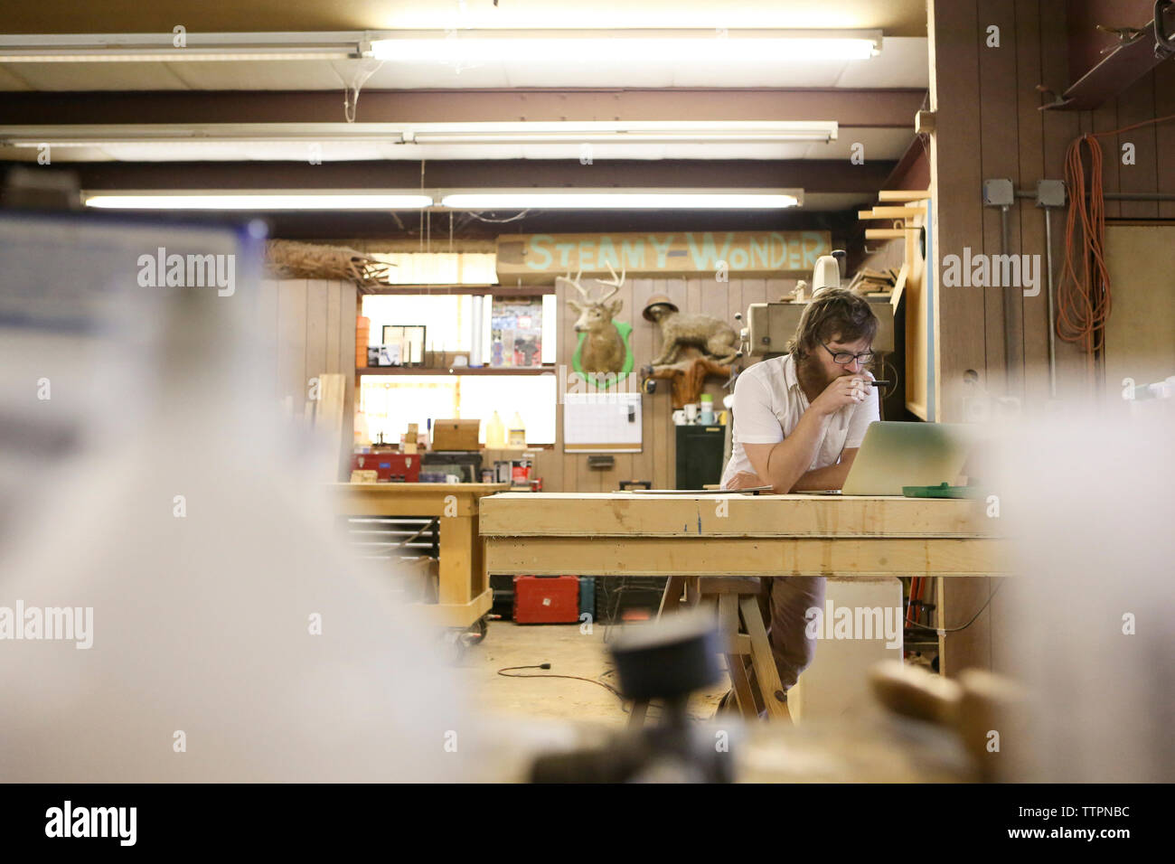 Carpenter using laptop computer while standing at table in workshop Stock Photo