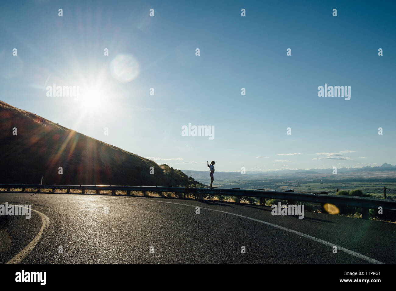 Side view of girl standing on railing by road against blue sky Stock ...