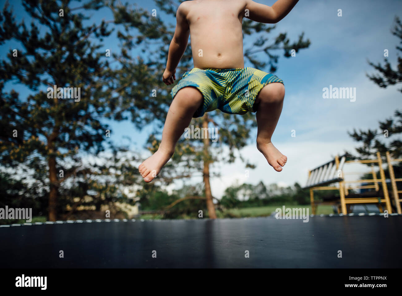 Low section of shirtless boy jumping on trampoline at park Stock Photo