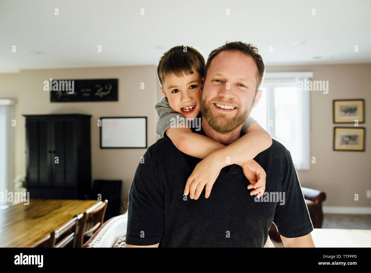 Portrait of father and son piggybacking while standing at home Stock Photo