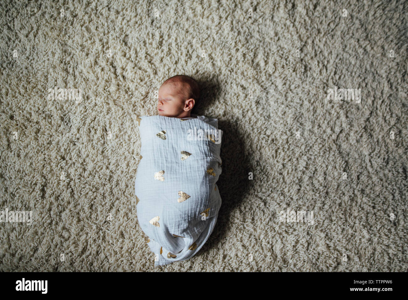 Overhead view of baby girl sleeping while being wrapped in blanket on