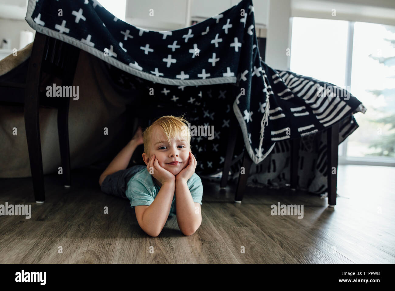 Portrait of confident boy with hands on chin lying under blanket tent at home Stock Photo