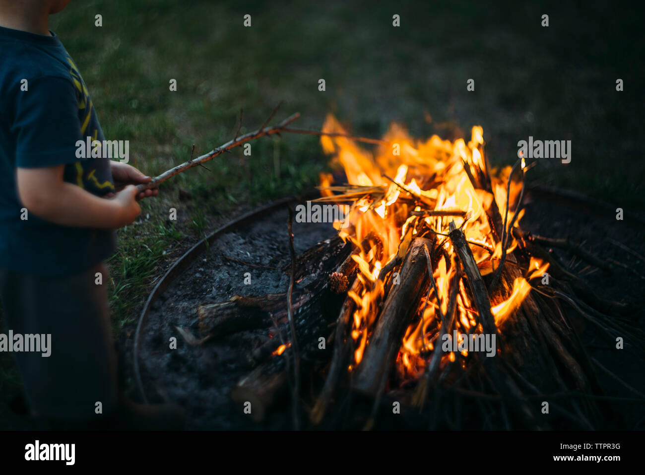 Midsection Of Boy Holding Stick While Standing By Fire Pit Stock
