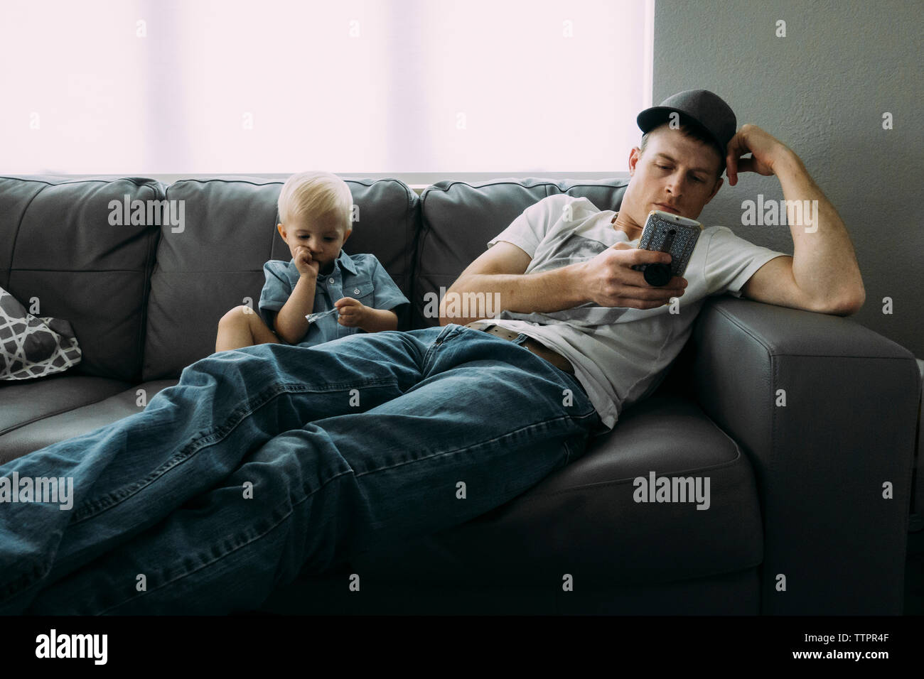 Father using phone while sitting by son on sofa at home Stock Photo