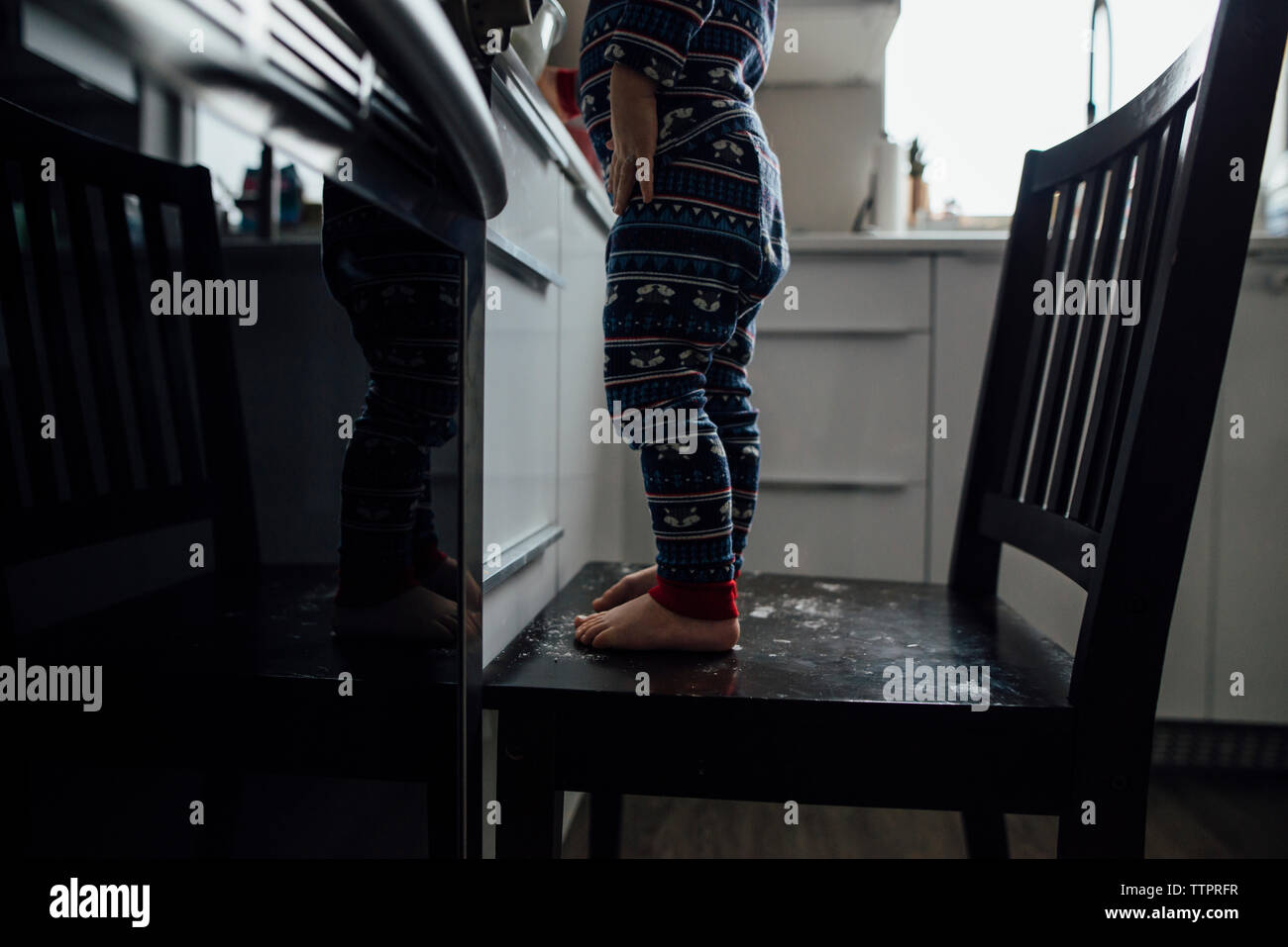 Low section of baby boy standing on chair in kitchen at home Stock Photo