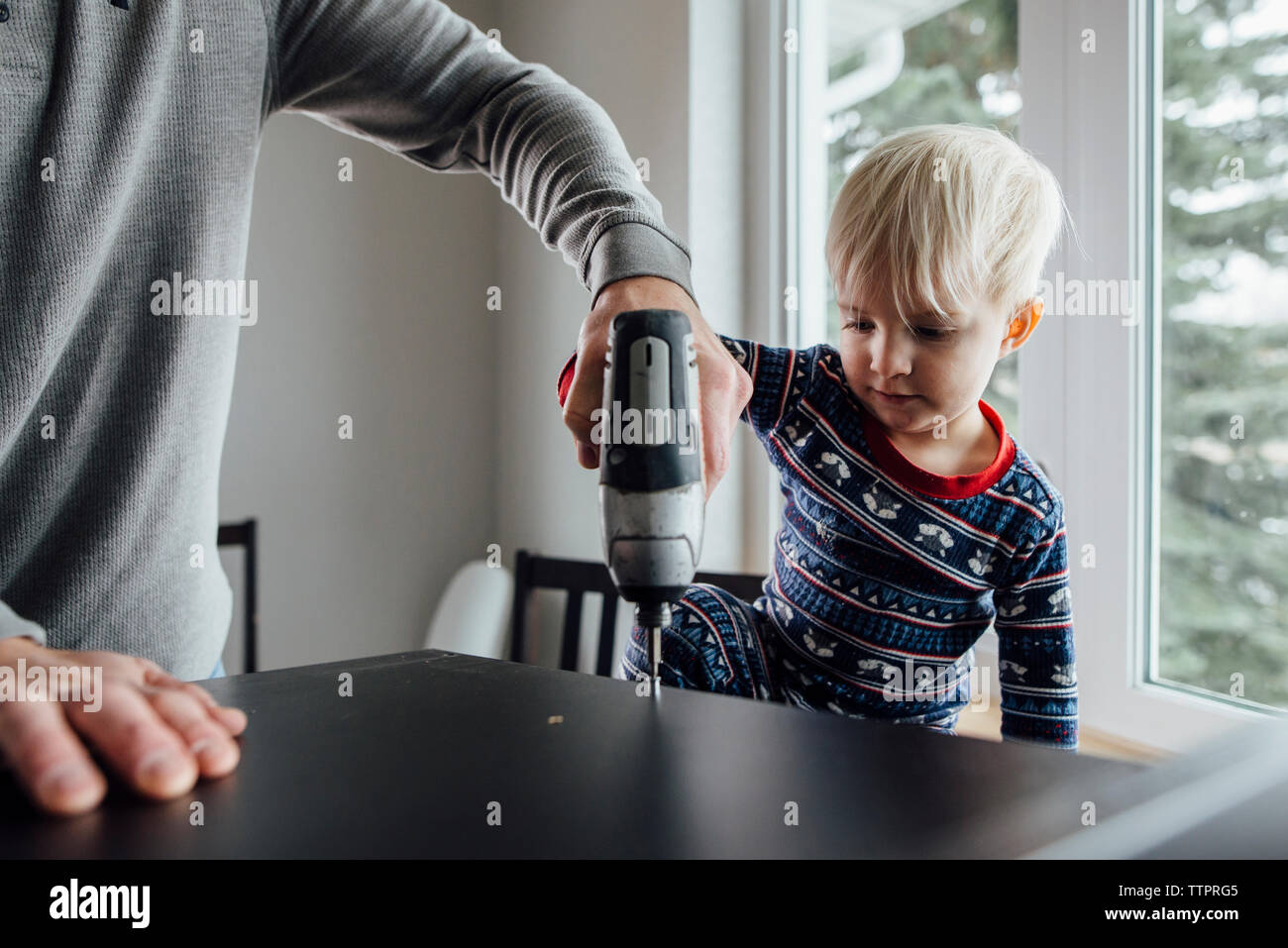 Midsection of father with son using drill on table at home Stock Photo