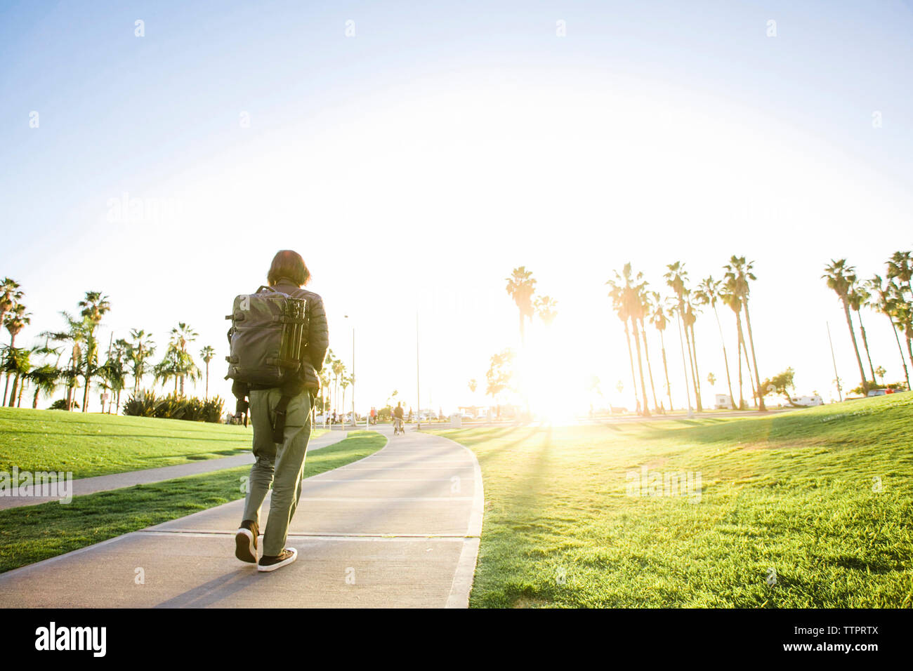 Rear view of man with backpack walking on footpath during sunny day ...